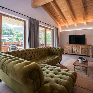 Ein Wohnzimmer mit grünem Sofa, Holzmöbeln und Blick auf die Terrasse bei den Alpegg Chalets